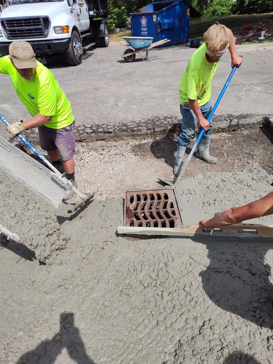 Crew placing concrete around a drainage inlet during flatwork installation