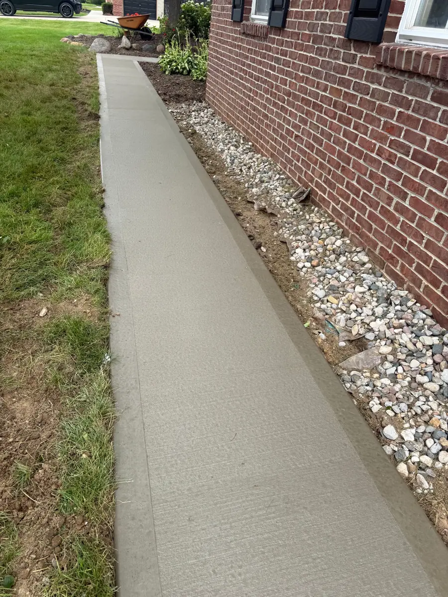 New narrow concrete walkway installed along a brick home